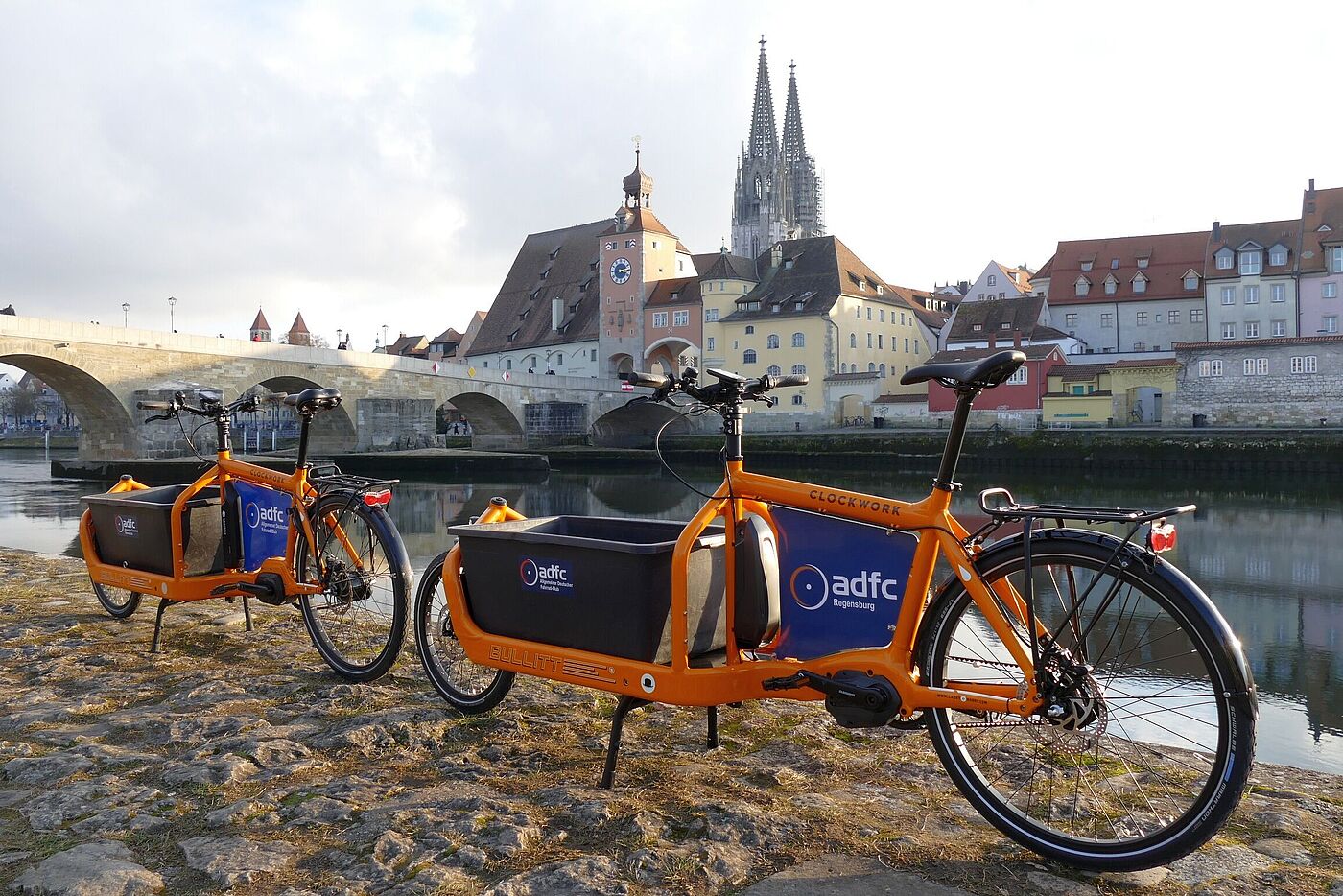 Zwei orange Lastenräder vor Steinerner Brücke und Silhouette Regensburg