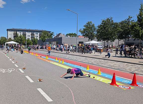 Kind malt auf Straße, im Hintergrund stehen viele Menschen