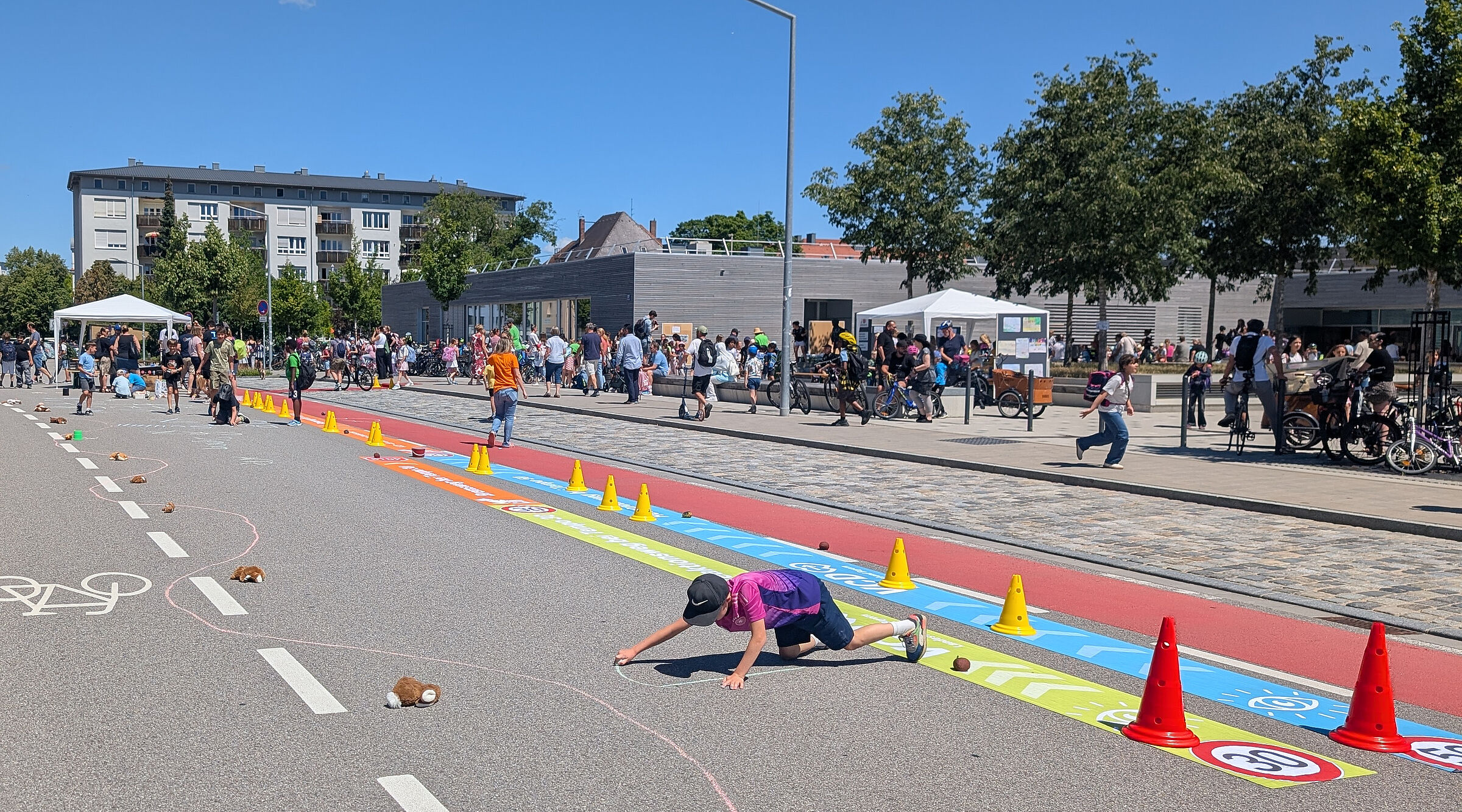 Kind malt auf Straße, im Hintergrund stehen viele Menschen