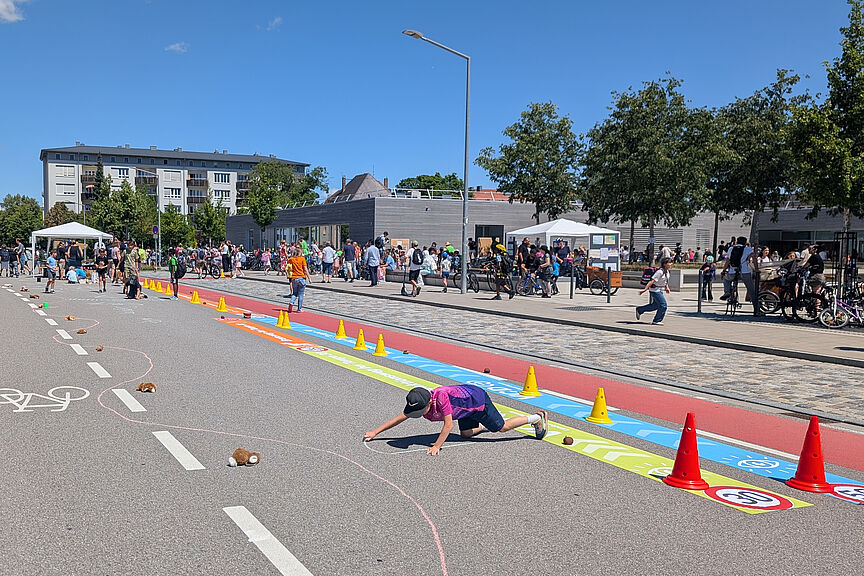 Kind malt auf Straße, im Hintergrund stehen viele Menschen