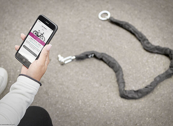 Person zeigt Smartphone mit "Gestohlen"-Anzeige vor offenem Fahrradschloss. Person zeigt Smartphone mit "Gestohlen"-Anzeige vor offenem Fahrradschloss.
